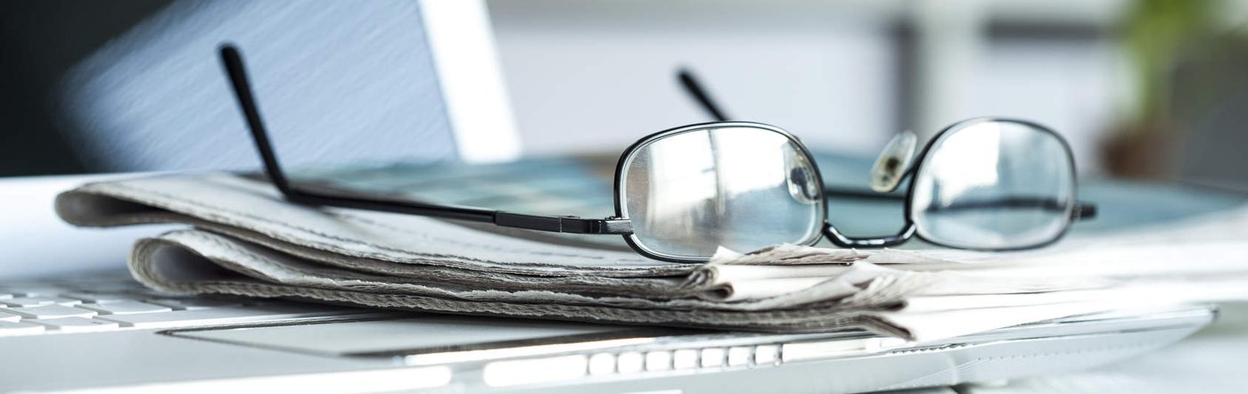 Zeitungen und Brille auf einem Schreibtisch